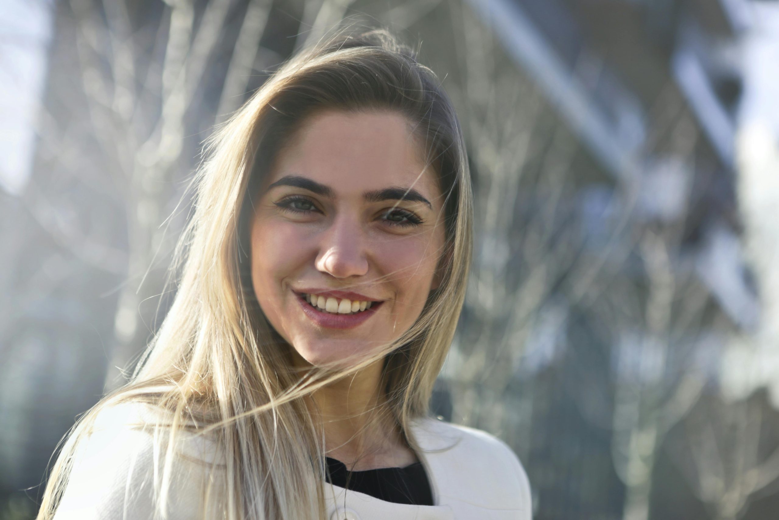 Portrait of a young woman smiling outdoors in a sunlit urban environment, radiating happiness.